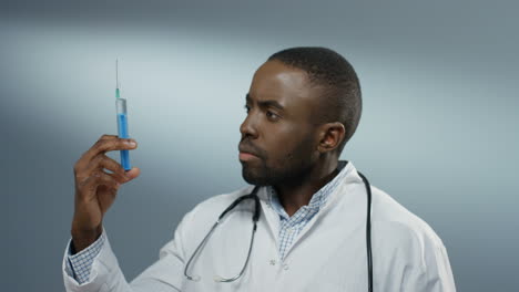 African-American-good-looking-young-male-doctor-or-intern-holding-a-syringe-with-a-needle-and-withdrawing-fluid-from-it.-Close-up.